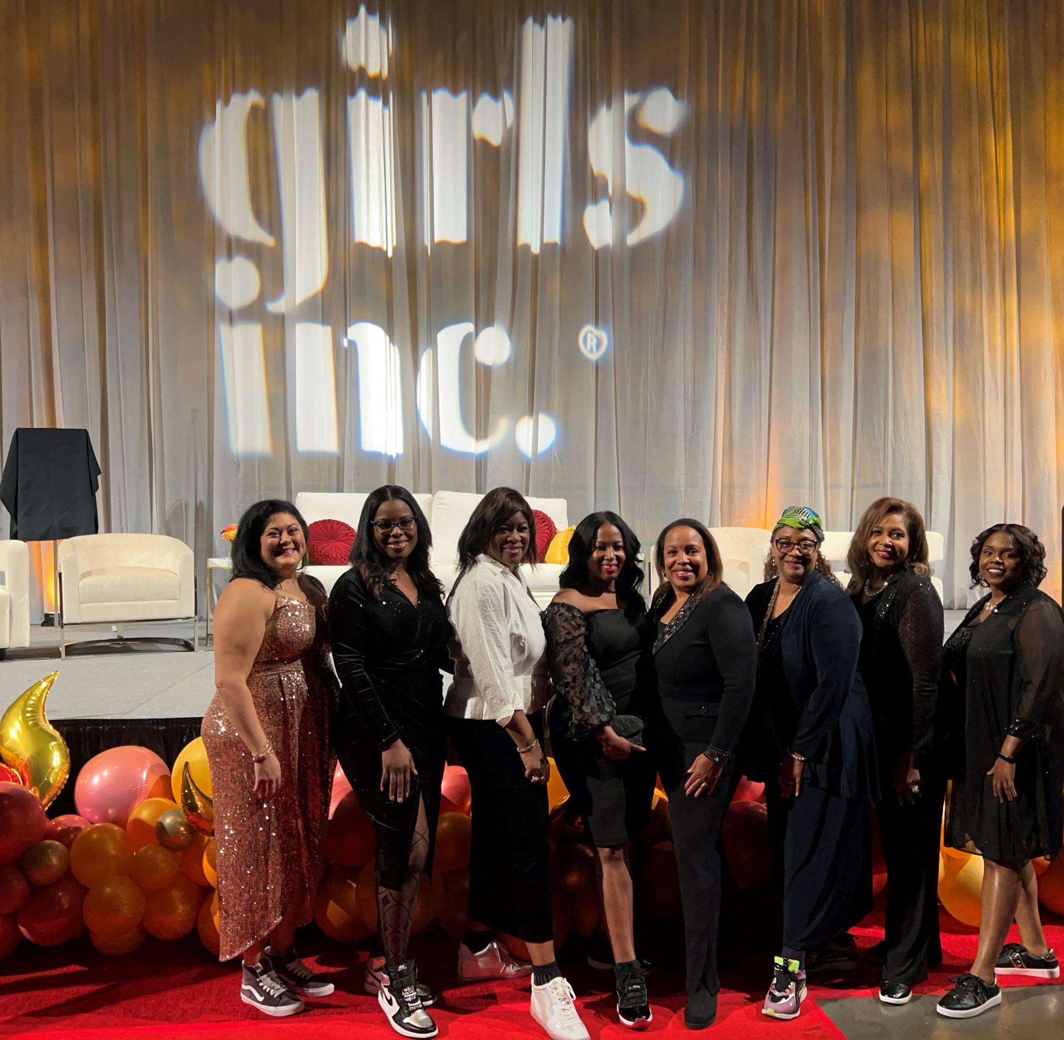 A group photo of eight woman, including Kimberly, standing in a group of women in front of a projection of the words, “Girls Inc.”